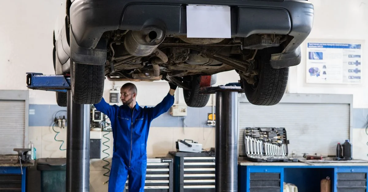 Mechaniker unter einem angehobenen Fahrzeug in einer hellen Werkstatt