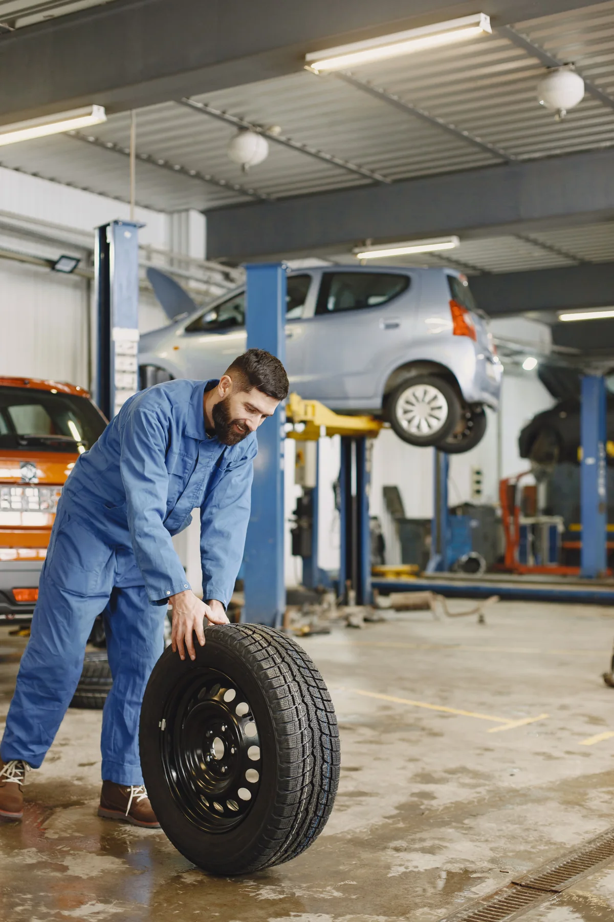 Mechaniker bewegt einen Reifen in einer Werkstatt mit Hebebühnen